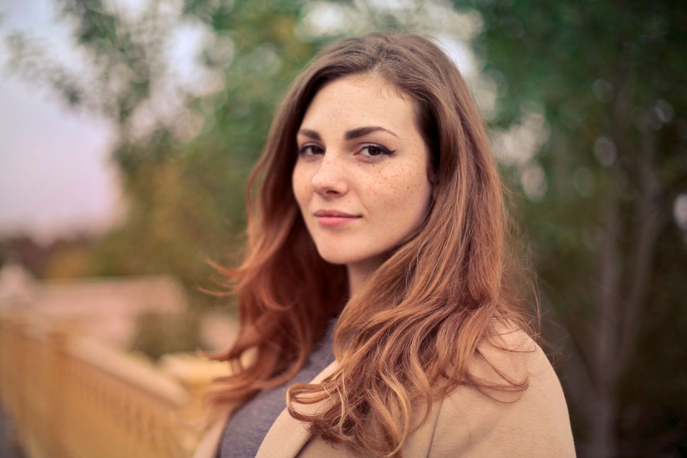 Žena stojí venku a dívá se před sebe.